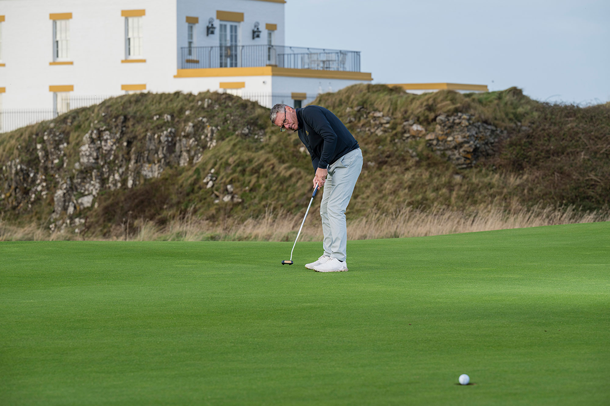 Steve North sinking a putt from around 25 feet on the 9th green at Turnberry, with the famous lighthouse in the background