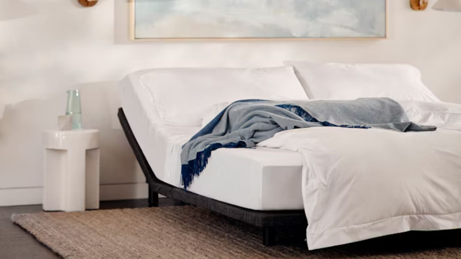 White sheets and gray blanket on the Casper Adjustable Base against white walls. 