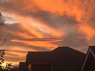 a saucer-shaped cloud hovers over a house against an orange-lit sky.
