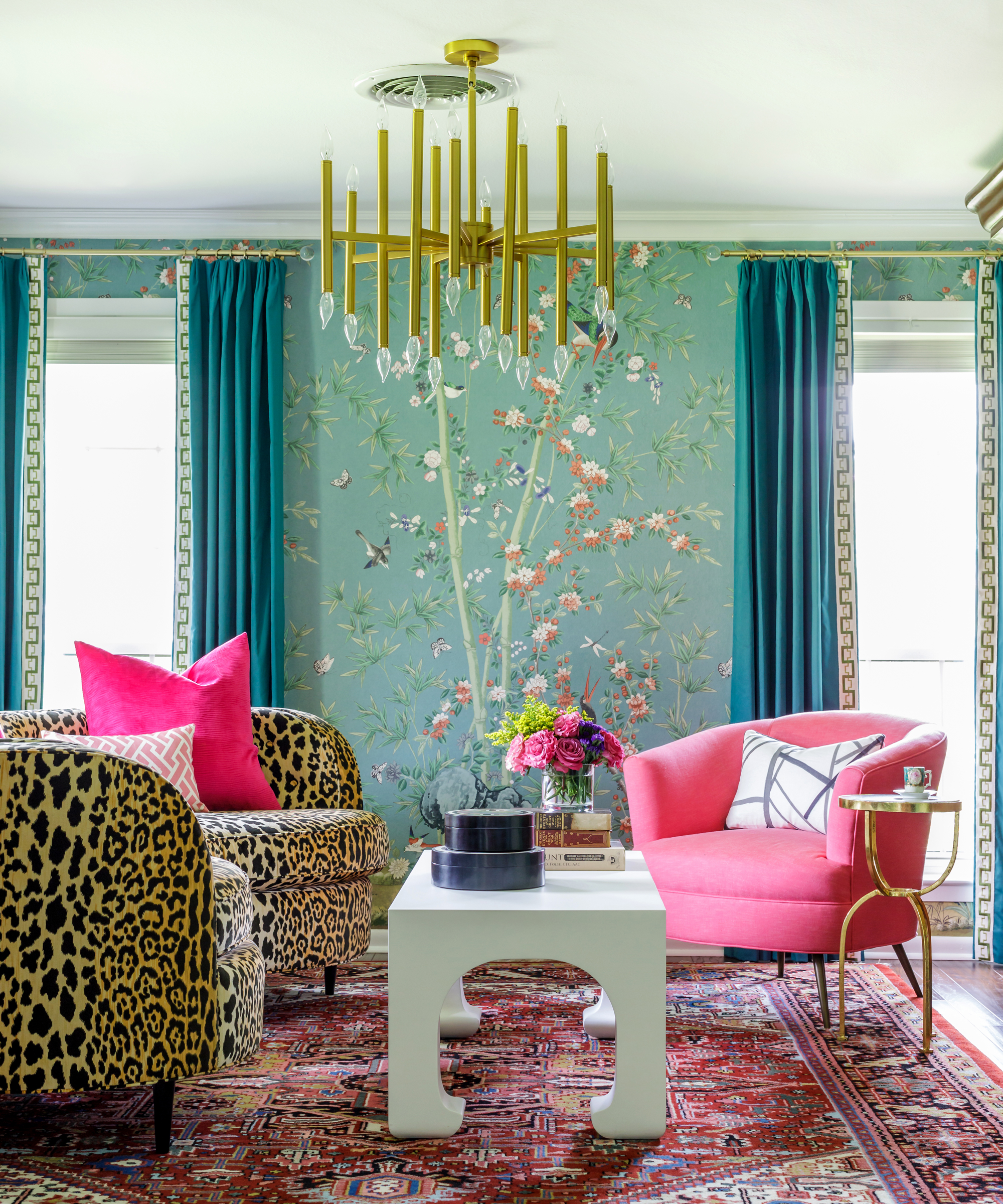 Glam, eclectic living room with chinoiserie wallpaper, hot pink chair, leopard print chairs, traditional rug, and brass statement pendant.