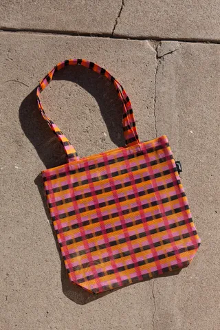 A geometrically designed, colorful tote bag in orange, brown, and pink stands against a cement wall.