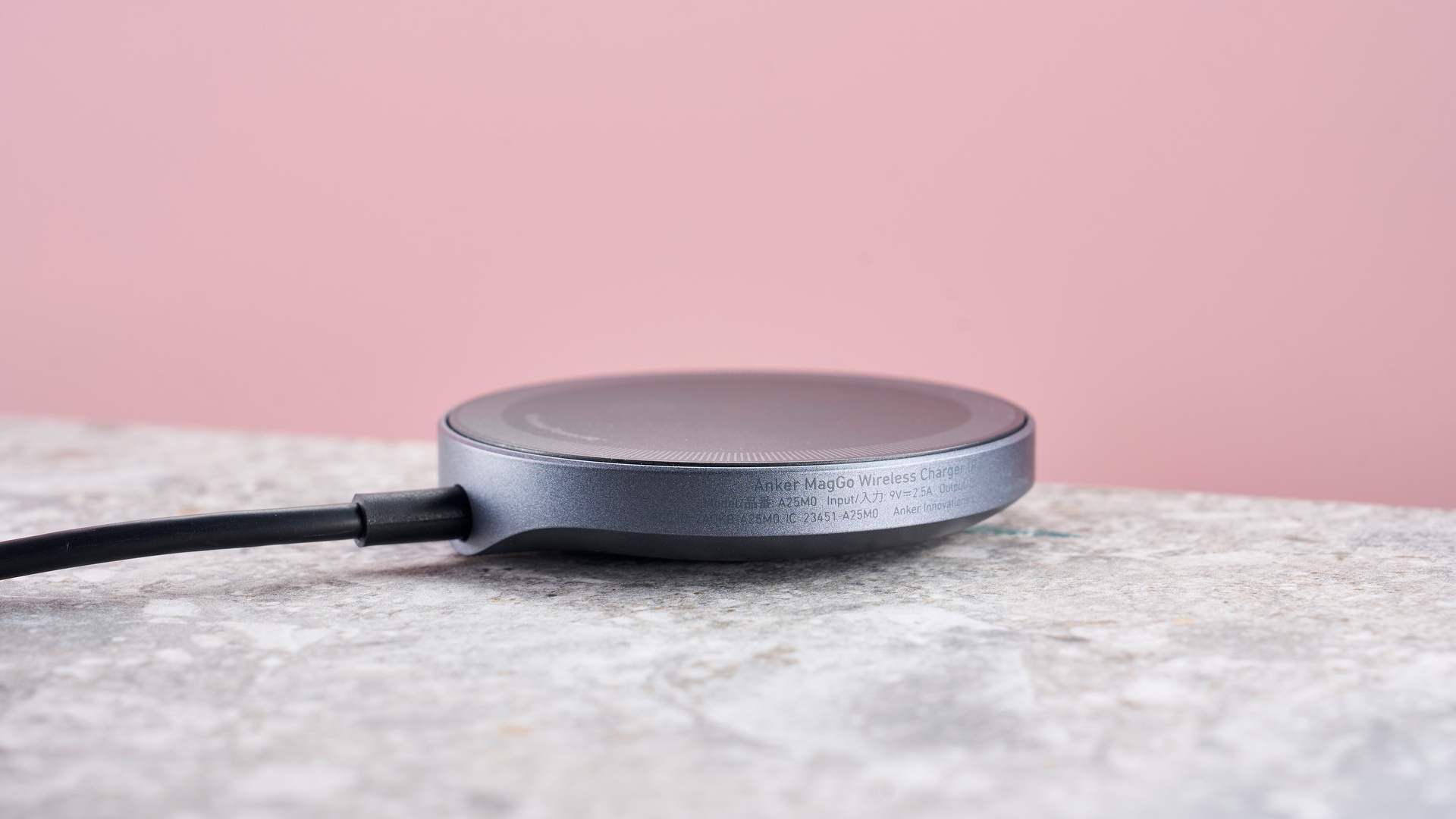 The side of the Anker Wireless Charging Pad, which is sitting on a grey stone-effect surface, against a light pink background.