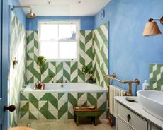 Blue painted bathroom with geometric green and white tiles, tiled wall and tiled bath, metal accessories