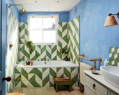 Blue painted bathroom with geometric green and white tiles, tiled wall and tiled bath, metal accessories