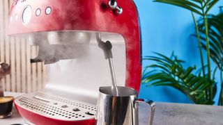 a red smeg espresso machine with burr grinder is photographed against a blue background