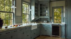 a warm mid-blue traditional kitchen with traditional crittal windows, corner glass front cabinet, detailed trim and marble counters
