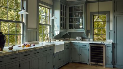 a warm mid-blue traditional kitchen with traditional crittal windows, corner glass front cabinet, detailed trim and marble counters
