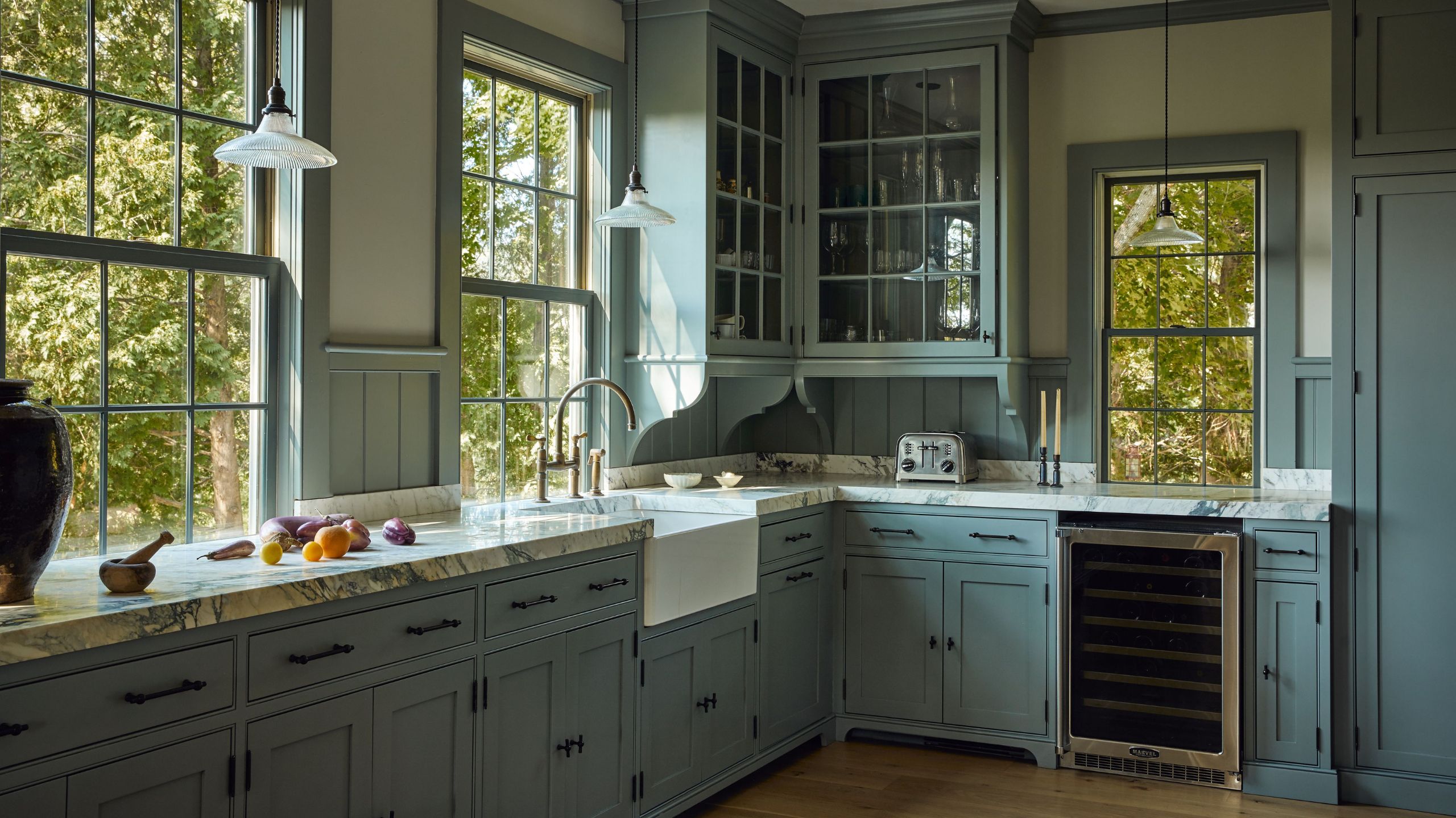 a warm mid-blue traditional kitchen with traditional crittal windows, corner glass front cabinet, detailed trim and marble counters