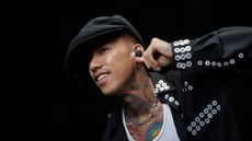 A young man wearing a black cap, jacket and white top is listening to Audio-Technica ATH-CKS50TW2 earbuds on a black background