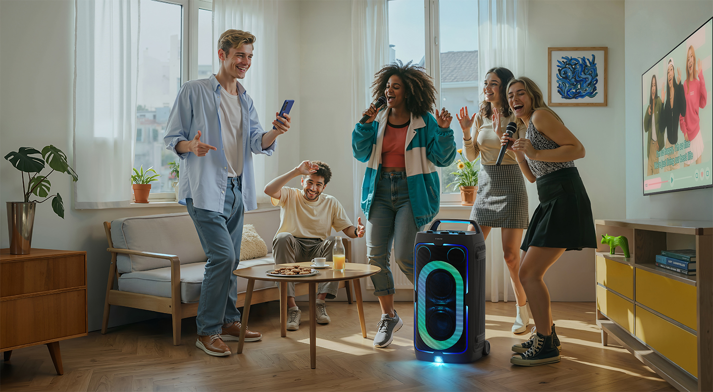 Five young people doing what looks like karaoke around a Samsung Sound Tower in a sunny apartment