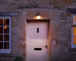 cottage with pale pink front door, singular light fixture above the front door