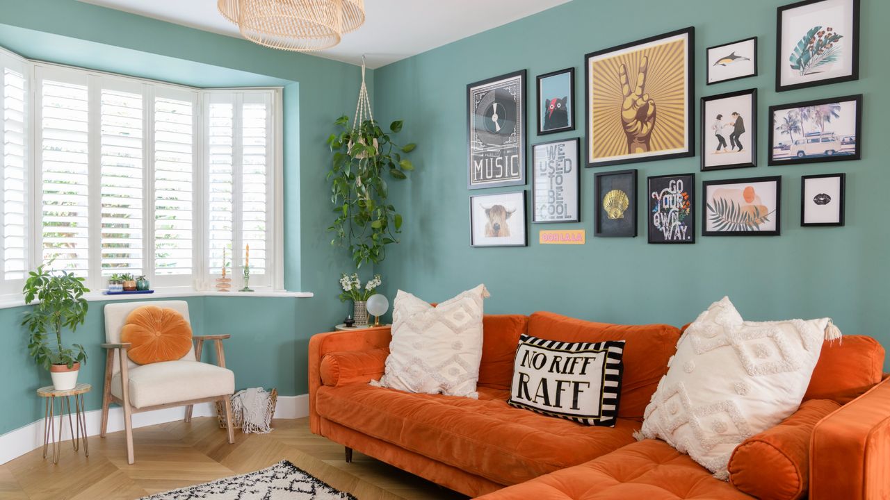 A mint green-painted living room with a chaise velvet orange sofa and a gallery wall display above it