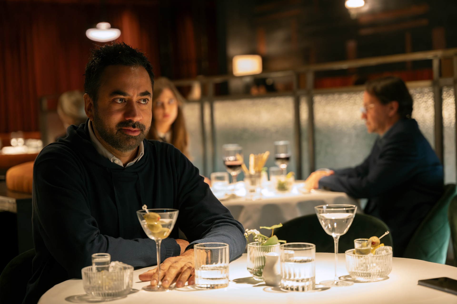 kal penn drinking a martini at a fancy restaurant in industry season 4