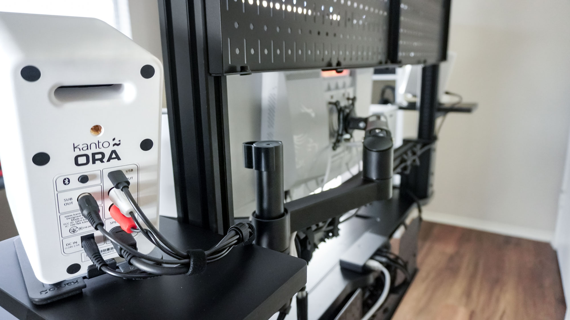 A rear shot of a black-and-white desk setup built around the Corsair Platform:4 Elevate Desk showing off the Kanto Ora bookshelf speakers and the cable management used in this project