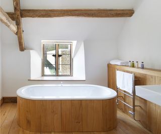 cottage bathroom with wood panelling on one wall, floor, around bath and exposed beams on ceiling