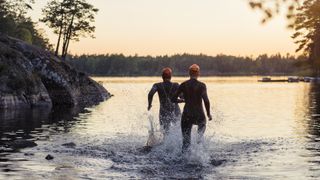 Two people in wetsuits running into the water at sunset