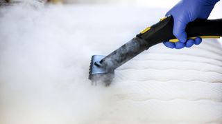 A steam cleaner going over a mattress with a cloud of steam over it