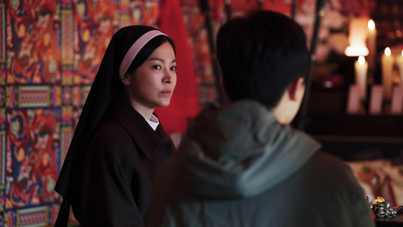 A nun (Song Hye-kyo) looks at an unseen boy as they sit in a colorful room, in the Korean movie 'Dark Nuns.'