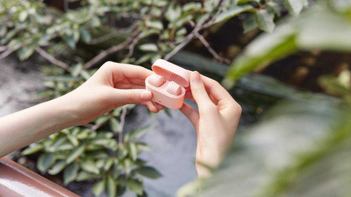 Woman holding Yamaha TW-EF3A Earbuds with plants in the background 