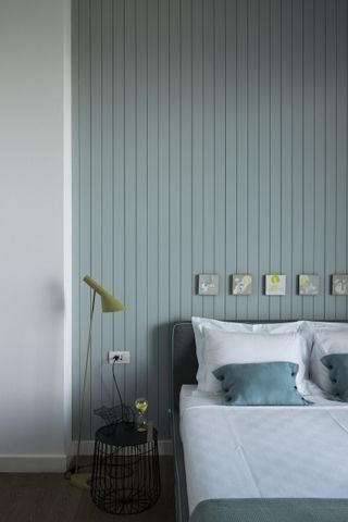A muted green themed bedroom with a sage green wood panelled accent wall