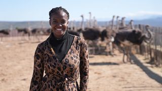 Oti Mabuse wearing leopard print blouse stood in front of Oudtshoorn Ostrich Farm in South Africa