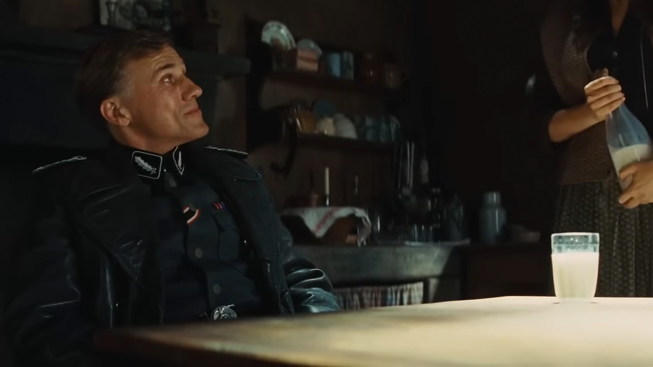 Christoph Waltz sitting, looking up with a glass of milk in front of him in Inglourious Basterds