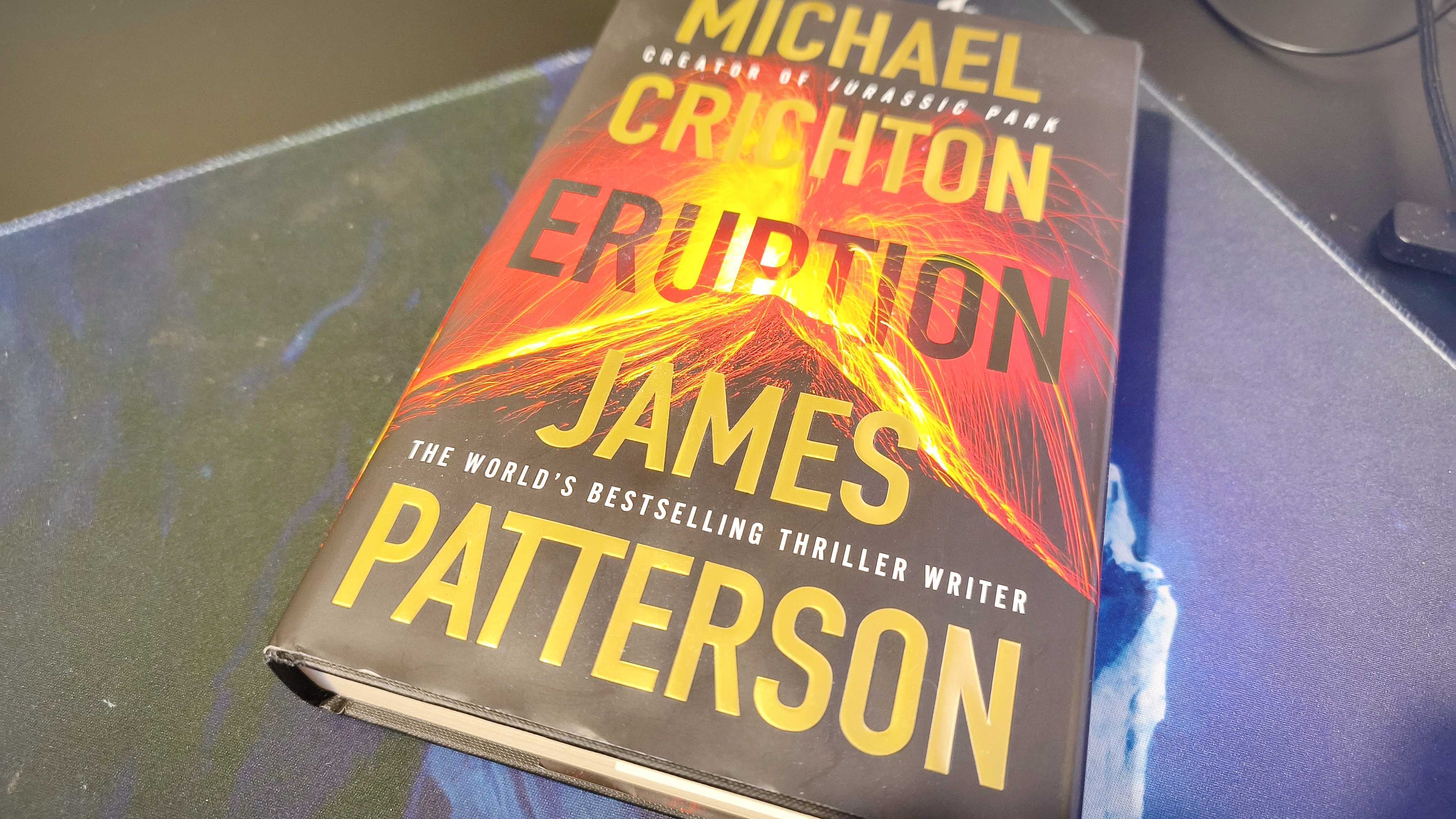 A book called Eruption by Michael Crichton and James Patterson sitting on a black desk