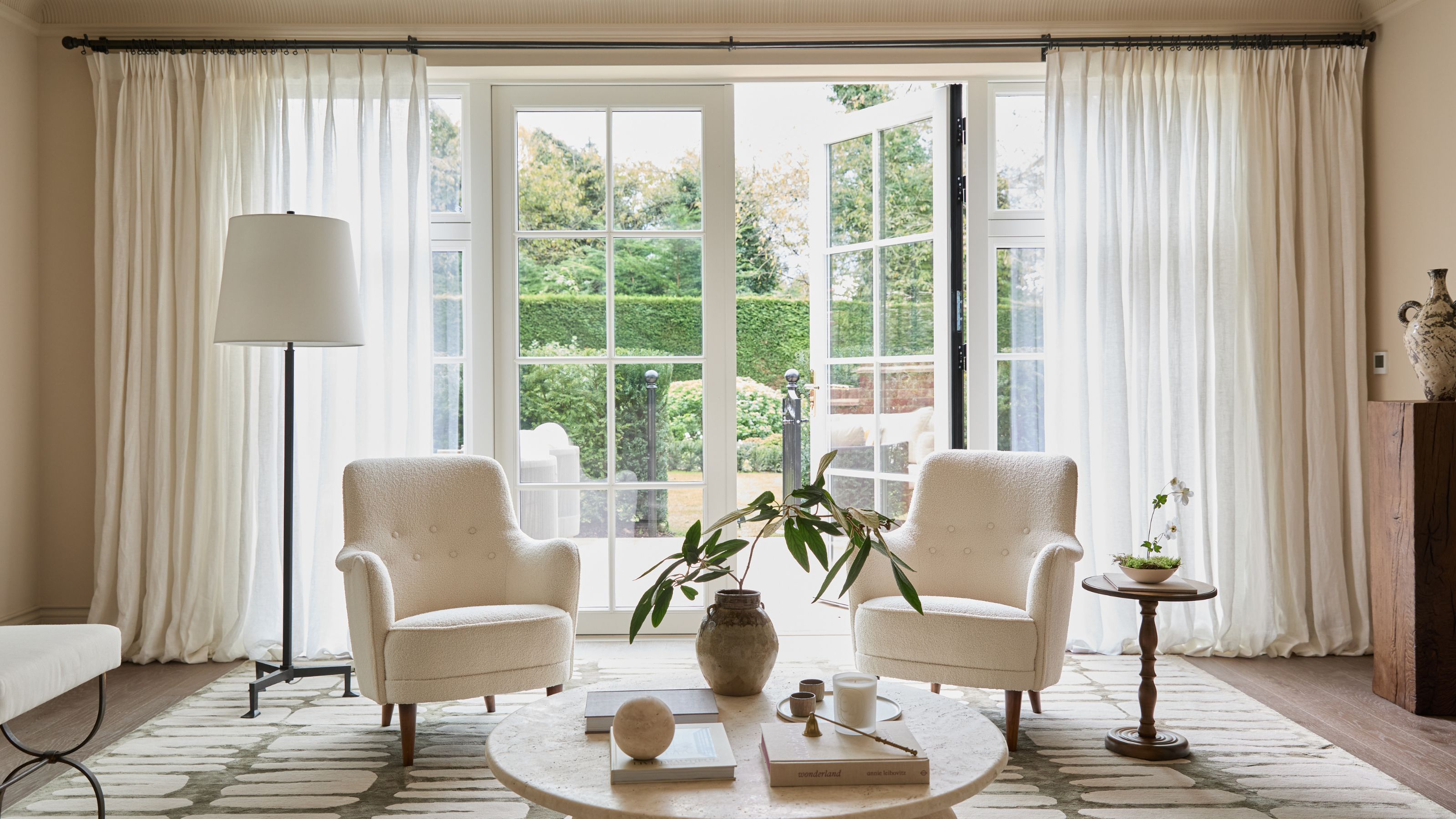 A modern living room with French doors, sheer curtains and neutral furnishings.