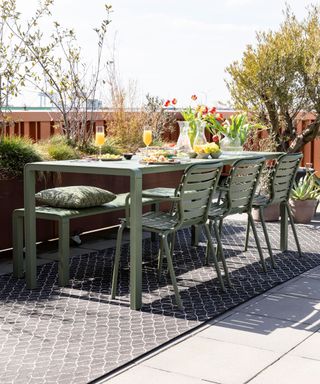 an outdoor terrace with a green dining table on a rug, to illustrate the worst patio decorating mistakes