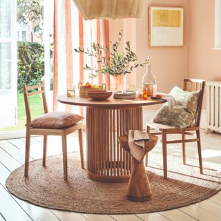 A soft peach-painted dining room with a round dining table and a round jute rug underneath