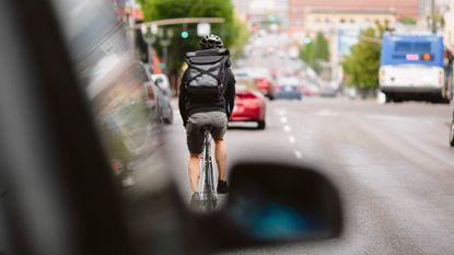 A cyclist on a street viewed over a car wing mirror