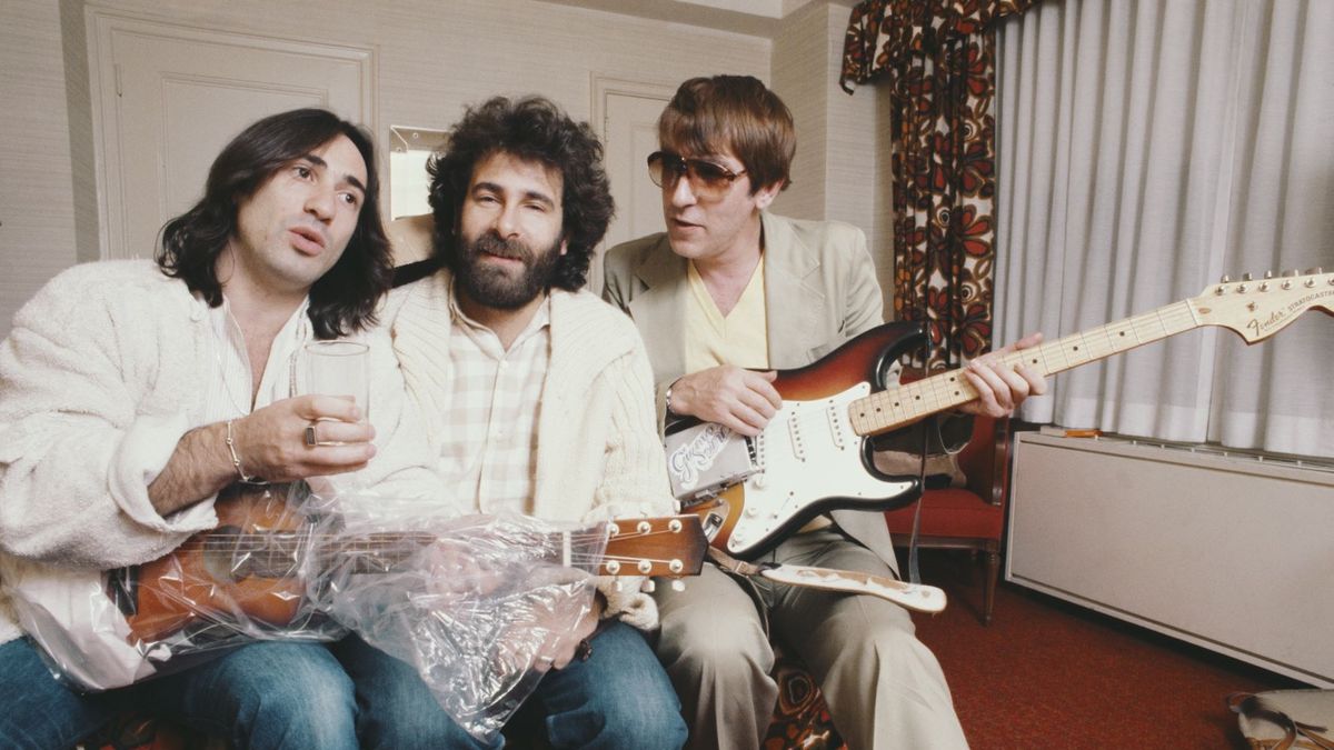 Lol Creme (left) and Kevin Godley (centre) from 10CC with English comedian Peter Cook (1937-1995), 1977. Cook is holding a Fender Stratocaster fitted with a prototype Gizmotron, (aka The Gizmo), an effects device invented by Godley and Cream, which uses serrated wheels to produce a bowing effect on guitar strings. Cook contributed to Godley and Creme&#039;s concept album &#039;Consequences&#039;, which was intended to showcase the Gizmotron. The device was later marketed commercially, but proved unsuccessful.