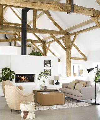a rustic living room with exposed beams, white walls, a gray floor and beige and gray sofas and armchairs, with a fireplace