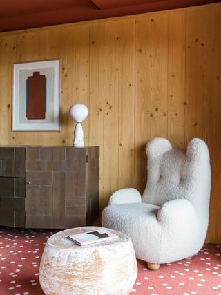 A whimsical hotel room features a cat-shaped shearling armchair, pois red and white carpeted floors, wood-paneled walls, and other arty touches.