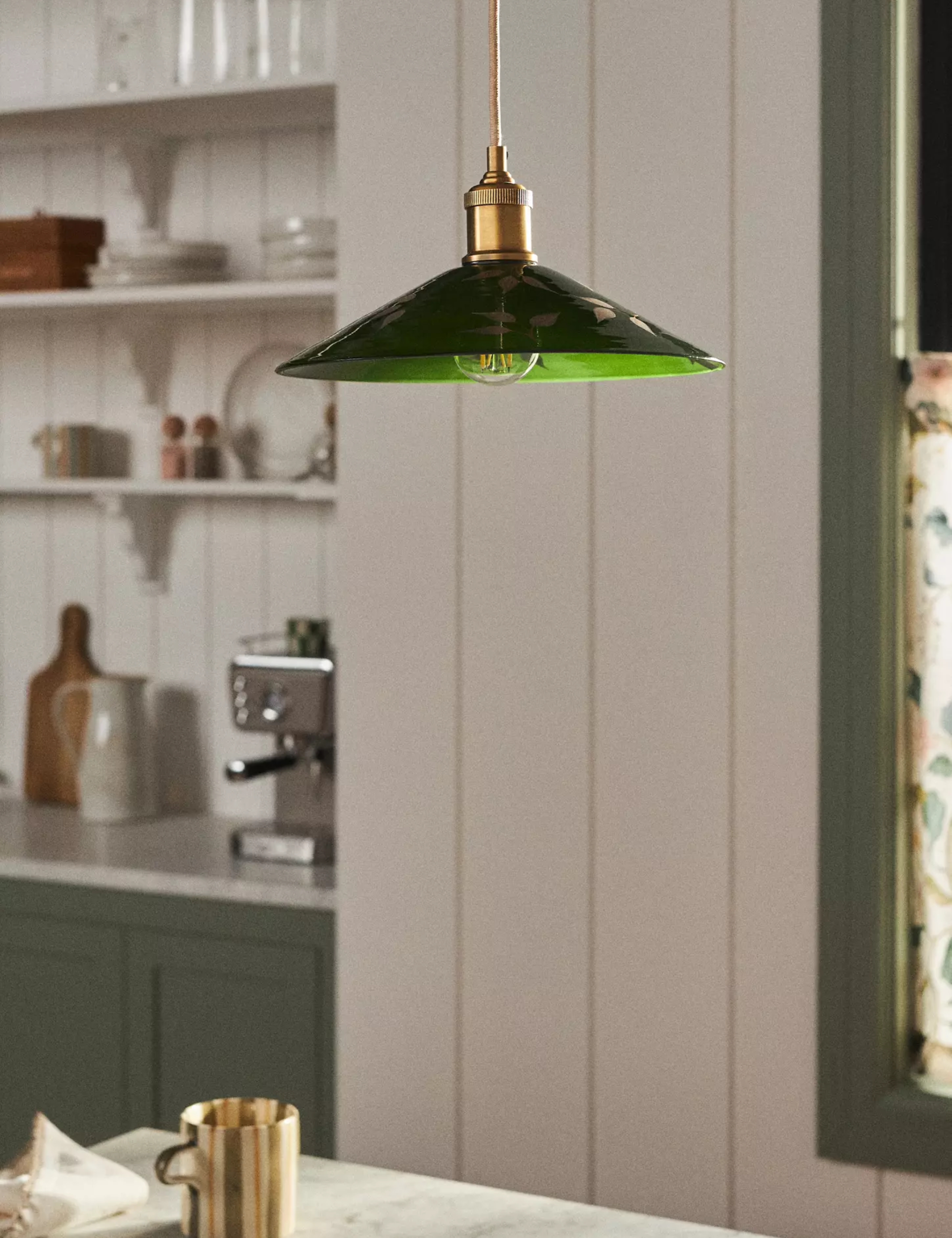 Anthropologie green glass pendant light painted with botanical motifs hanging inside of a charming white breakfast nook