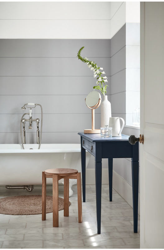 A grey bathroom with wall panelling behind a white roll top bath