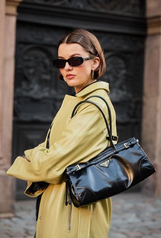 a photo of a woman wearing a green leather trench coat and a vintage prada bag from a luxury resell site