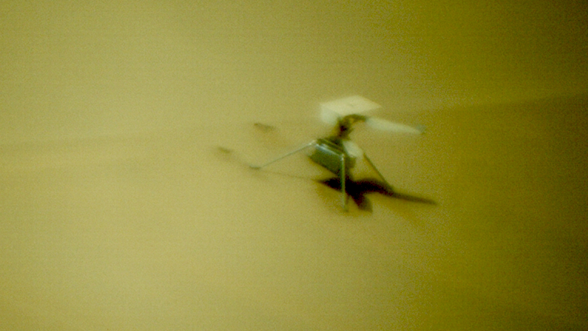 close-up view of a small, boxy drone resting on a sand dune.