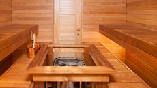 A picture of the inside of a sauna with a central stove, bucket and ladle.