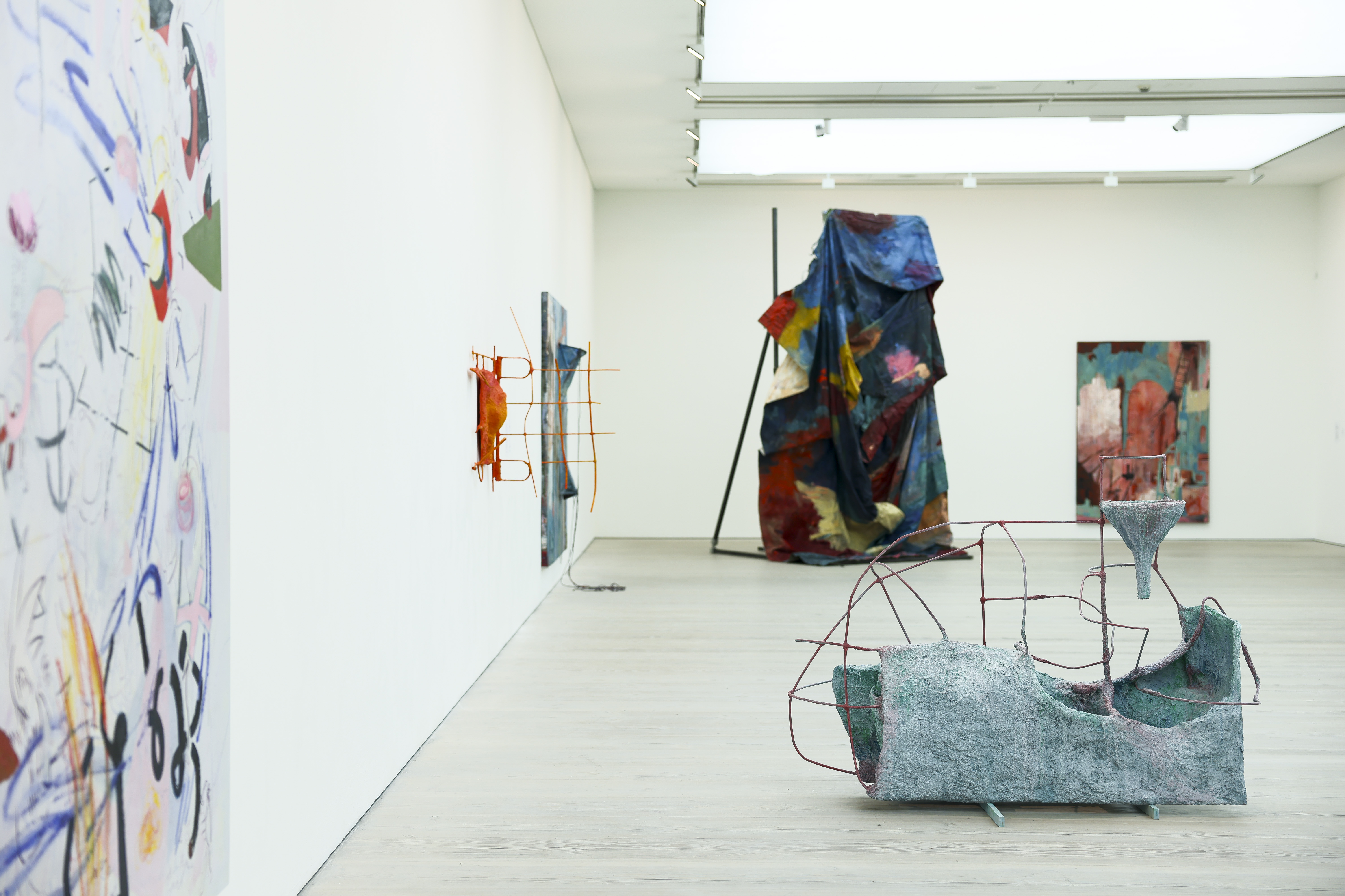 A gallery room filled with large sculptural works in colorful fabric and iron, as well as vibrant canvases.