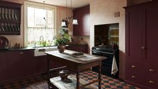 A small burgundy kitchen with small checkerboard floor tiles and a work table island
