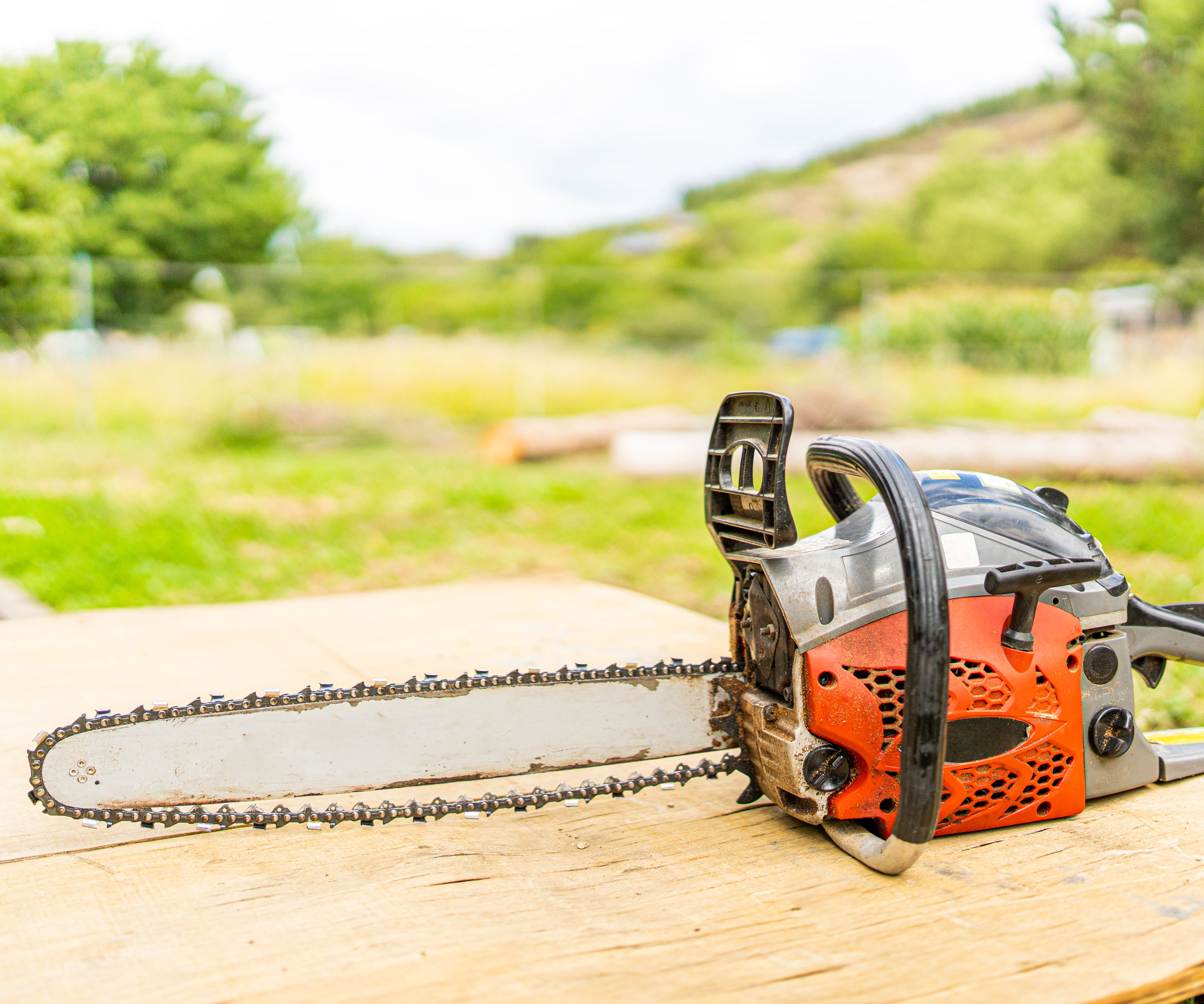 chainsaw sitting idle on wooden surface against grassy backdrop
