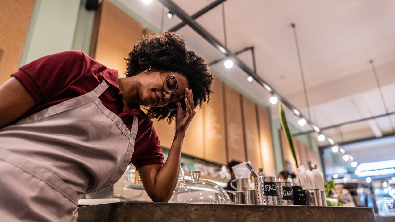 A clearly frustrated waitress leans on a counter in a restaurant.