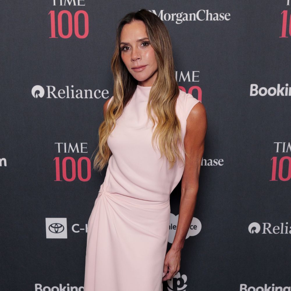 Victoria Beckham poses for a photo wearing a pale pink dress with red pointed-toe sandal heels.