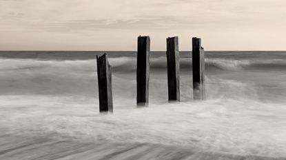 A damaged groyne on a UK beach, the high tide is smashing into it, with the moving water blurred using a long exposure photography technique