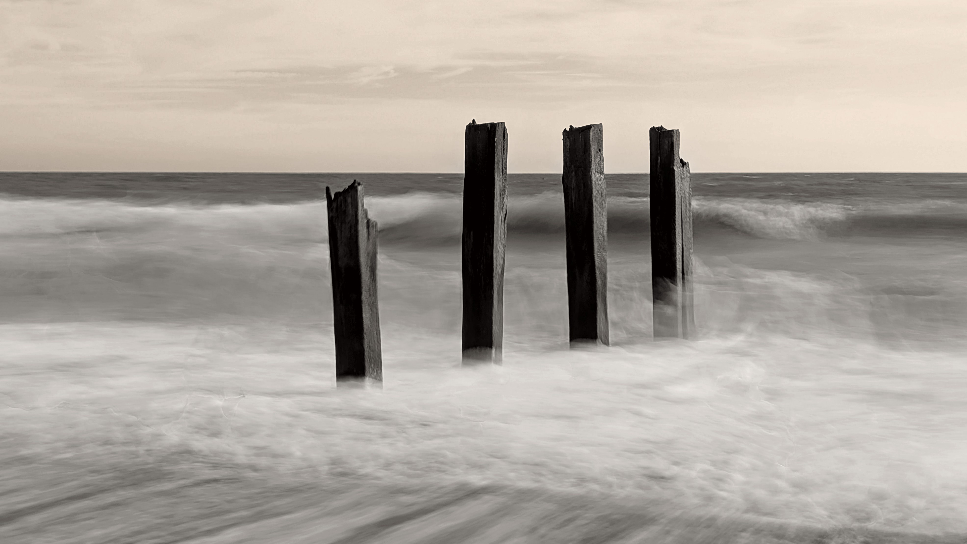 A damaged groyne on a UK beach, the high tide is smashing into it, with the moving water blurred using a long exposure photography technique