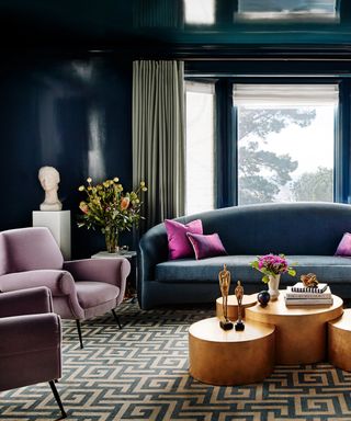 Blue living room with blue walls, woodwork and ceiling, lilac accents, blue couch, gold metallic coffee table nest, drapes