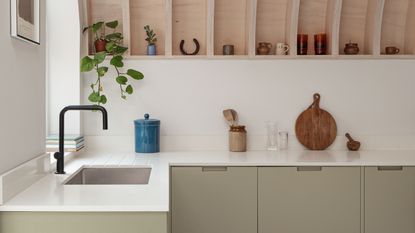 A kitchen with sage green slab cabinets, a wooden vaulted ceiling, and a white quartz countertop 