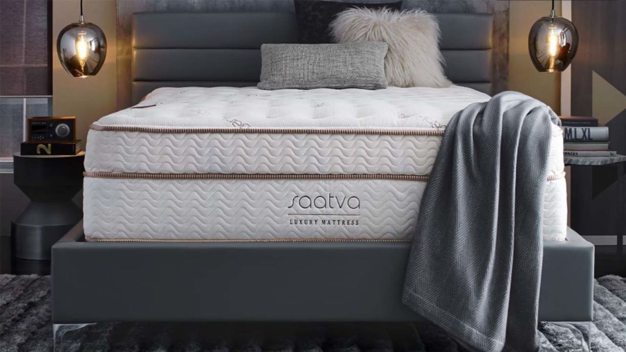 A blanket and throw pillows on the Saatva Classic Mattress on a gray bed frame.