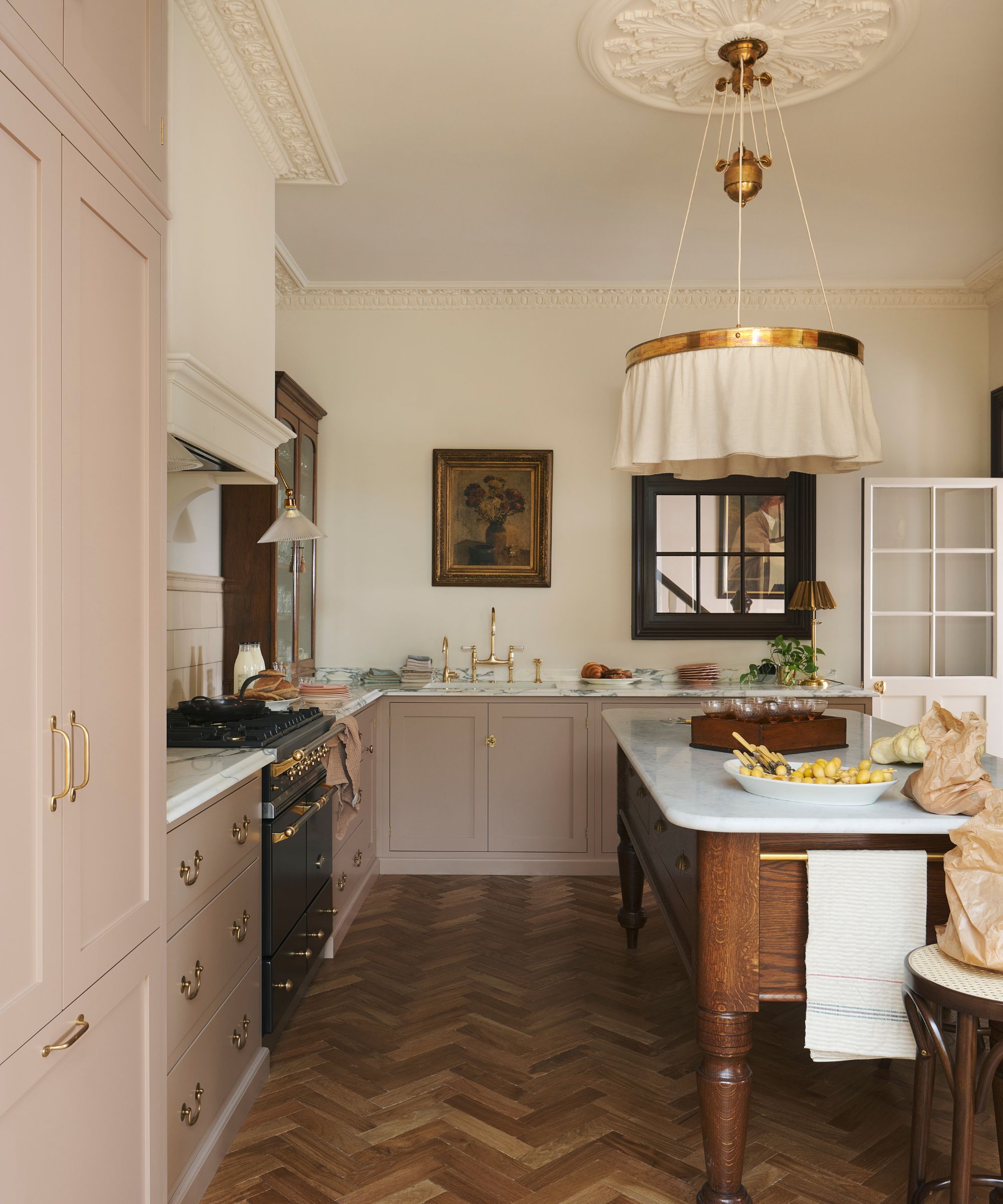 A Victorian kitchen with pink cabinets, cream walls, and a freestanding wooden island